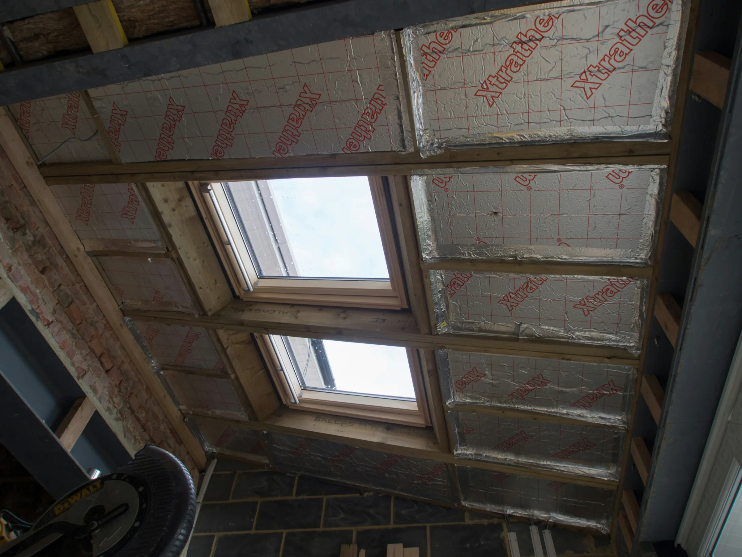 Ceiling under construction with two skylights and red "Knauf" branded insulation batts installed between wooden framing.